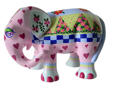 Hand-painted pink resin elephant figurine with red hearts, floral details, a blue checkerboard band, and a colourful patchwork rug from the Painted Pigs collection